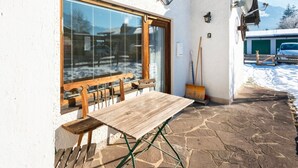 A wooden bench and table outside a building with a stone floor, a window with blinds, and a satellite dish. - Traditional Bungalow in Kitzbuhel Alps (Kirchdorf in Tirol)