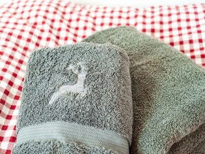 Una toalla gris doblada con un diseño bordado en blanco sobre un edredón de cuadros rojos y blancos.