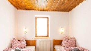 A room with two single beds, each with a checkered bedspread and matching pillows, a radiator, and two wall-mounted light fixtures. - Traditional Bungalow in Kitzbuhel Alps (Kirchdorf in Tirol)