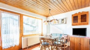 A cozy dining area with a wooden table, chairs, and a blue patterned sofa. A wooden cabinet with a TV is against the wall. - Traditional Bungalow in Kitzbuhel Alps (Kirchdorf in Tirol)