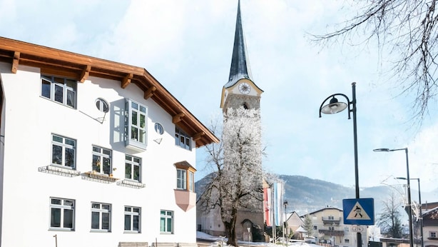 A building with a clock tower, a street lamp, and a pedestrian crossing sign. - Traditional Bungalow in Kitzbuhel Alps (Kirchdorf in Tirol)