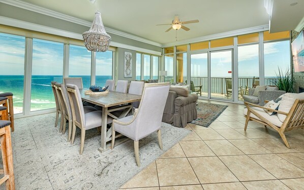 A spacious room with a large dining table, comfortable seating, a chandelier, and a view of the ocean. - Phoenix Orange Beach 1906 4 Bedroom Condo (Orange Beach)
