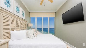 A bedroom with a bed, a ceiling fan, a TV, and a view of the ocean. - Phoenix Orange Beach 1906 4 Bedroom Condo (Orange Beach)