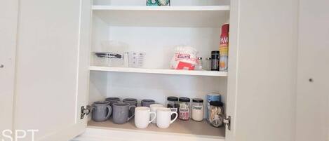 A kitchen cabinet with shelves containing various kitchen items such as coffee mugs, containers, and spices.