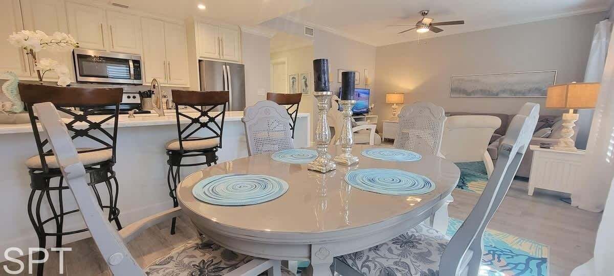 A dining area with a round table, chairs, and a central decorative piece. There is a kitchen area with cabinets and appliances in the background.