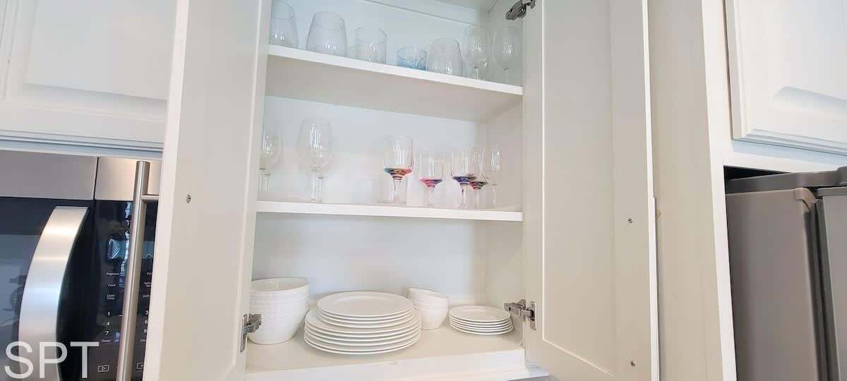 Een keuken met witte kasten, een roestvrijstalen koelkast en planken met wijnglazen en borden.
