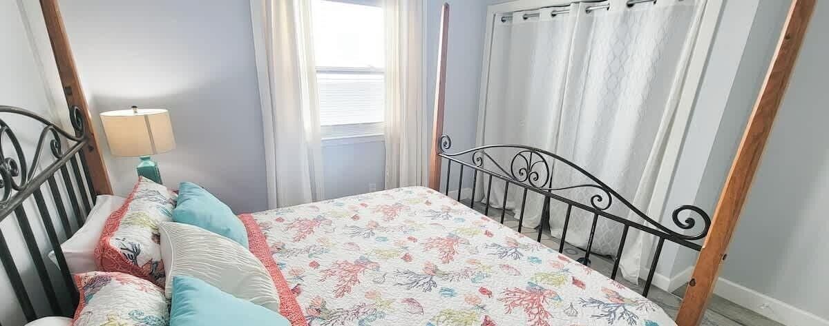 A bedroom with a four-poster bed, a bedside table with a lamp, and a window with curtains.