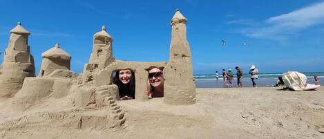 A sandy beach with a large sandcastle featuring multiple towers and a central structure.