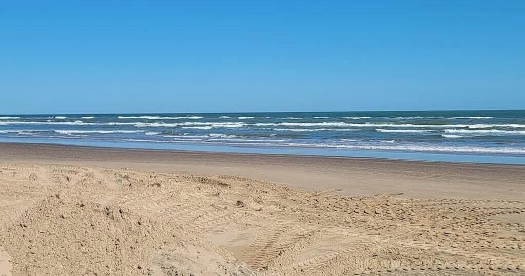 Een strand met duidelijke sporen van banden en voetafdrukken in het zand, die naar de oceaan leiden.