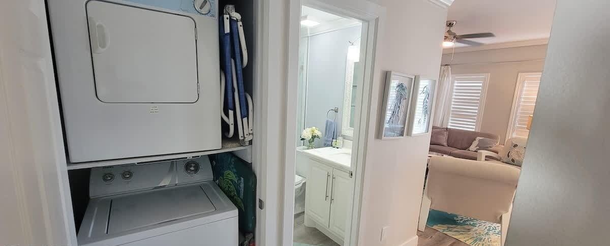 Un área de lavandería con lavadora y secadora, un baño con lavamanos y espejo, y una sala de estar con sofá y ventilador de techo.