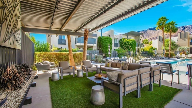 A covered outdoor area with seating, a pool, and a view of buildings and mountains.