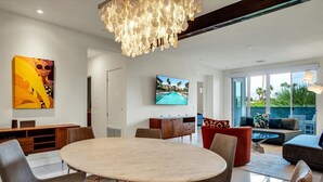 A modern living room with a round table, comfortable seating, a large TV, and a view of the outdoors.