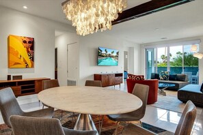 Uma sala de estar moderna com uma mesa redonda, assentos confortáveis, uma televisão grande e vista para o exterior.