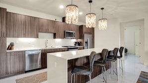 A modern kitchen with a central island, bar stools, and pendant lighting.