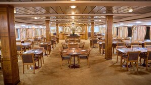 Un vaste espace dédié à la salle à manger, avec plusieurs tables et chaises rondes, des piliers en bois et une fontaine décorative au centre.
