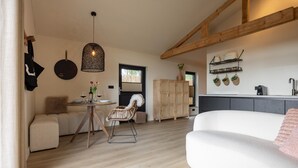 Una sala moderna con un sofá blanco, una mesa de comedor de madera y una silla de mimbre. Hay una zona de cocina con encimera gris y armarios de madera.