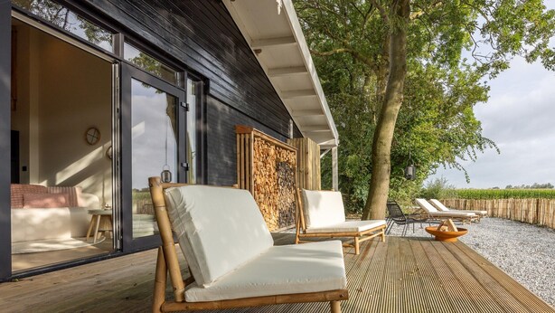 Terraza de madera con dos sillas blancas acolchadas y una pequeña mesa, con vista a un cuerpo de agua.