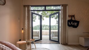Un dormitorio con un gran ventanal corredera que da a una terraza exterior, una silla de mimbre, una pequeña mesa redonda y un letrero con la palabra 'LOVE' en la pared.