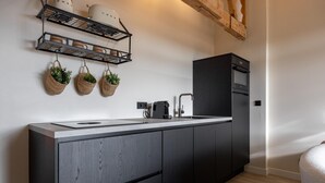 Una cocina moderna con estufa integrada, cafetera y refrigerador negro. Hay tres cestas colgantes con plantas en la pared sobre la encimera.