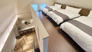 Et moderne hotelværelse med loftstil, der indeholder to senge, et lille skrivebord og et rundt vindue.