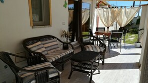 Un patio con mobiliario de mimbre, incluyendo un sofá y sillas, una mesita y una planta en maceta.