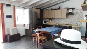 Cocina compacta con comedor, que incluye una mesa con mantel a cuadros, sillas de madera y un sombrero blanco sobre una encimera.