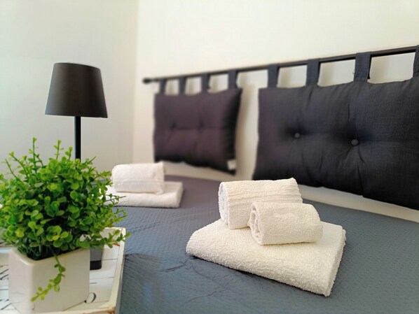 A neatly made bed with folded white towels, a black lamp, and a potted plant on a bedside table.