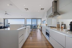 A modern kitchen with a central island, a stove, and a range hood. There is a dining area with a table and chairs, and large windows offering a view.