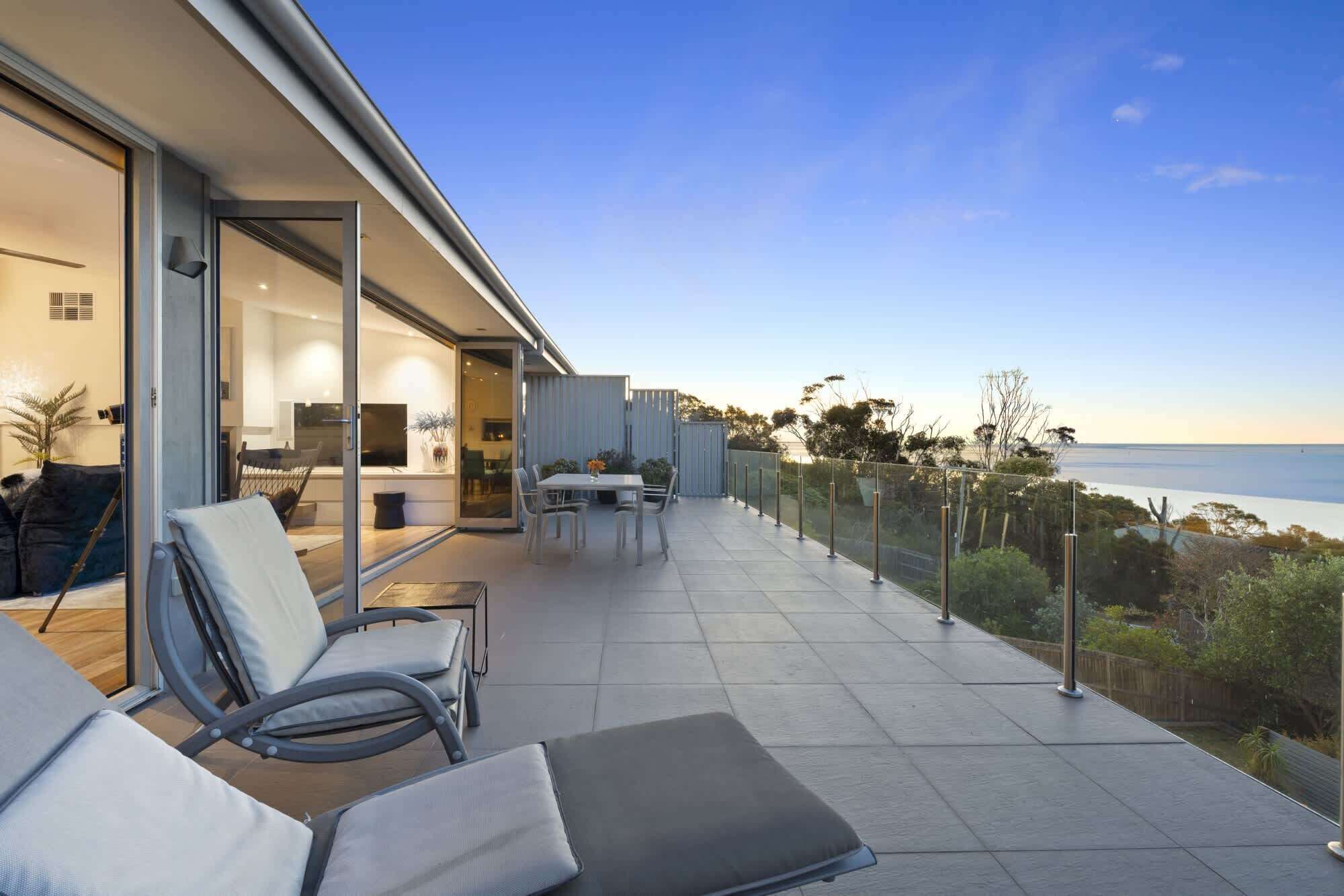 A modern outdoor patio with a dining area, seating, and a view of the sea.