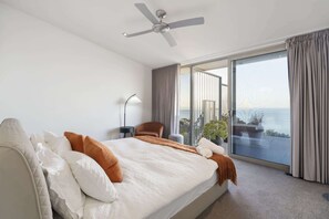 Ein Hotelzimmer mit einem großen Bett, einem Deckenventilator, einer Stehlampe und Meerblick durch große Schiebetüren.