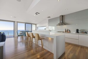 A modern kitchen with a large island, bar stools, and a view of the ocean.