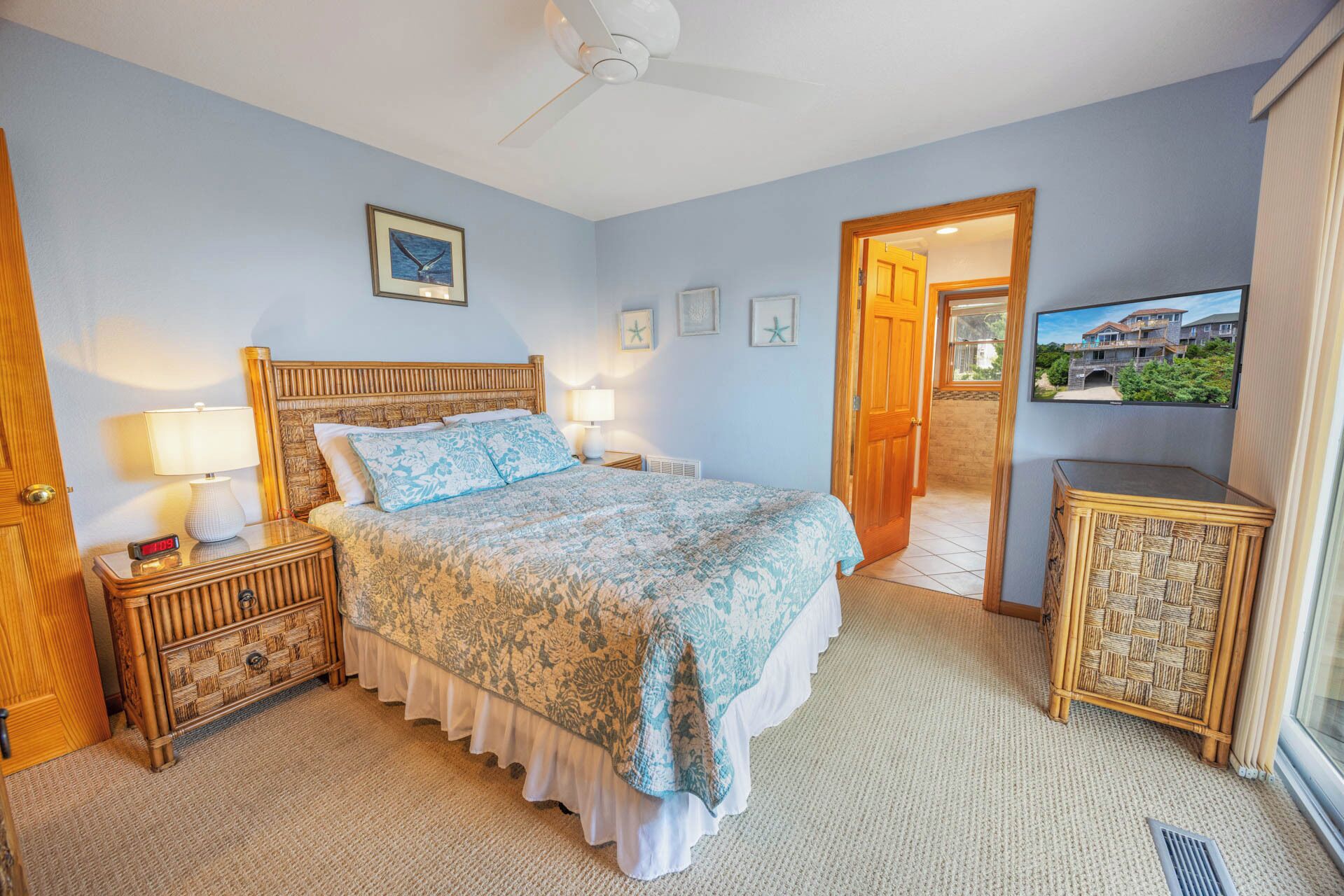 A bedroom with a bed, bedside tables, a nightstand, a ceiling fan, a TV, and a door leading to a balcony.