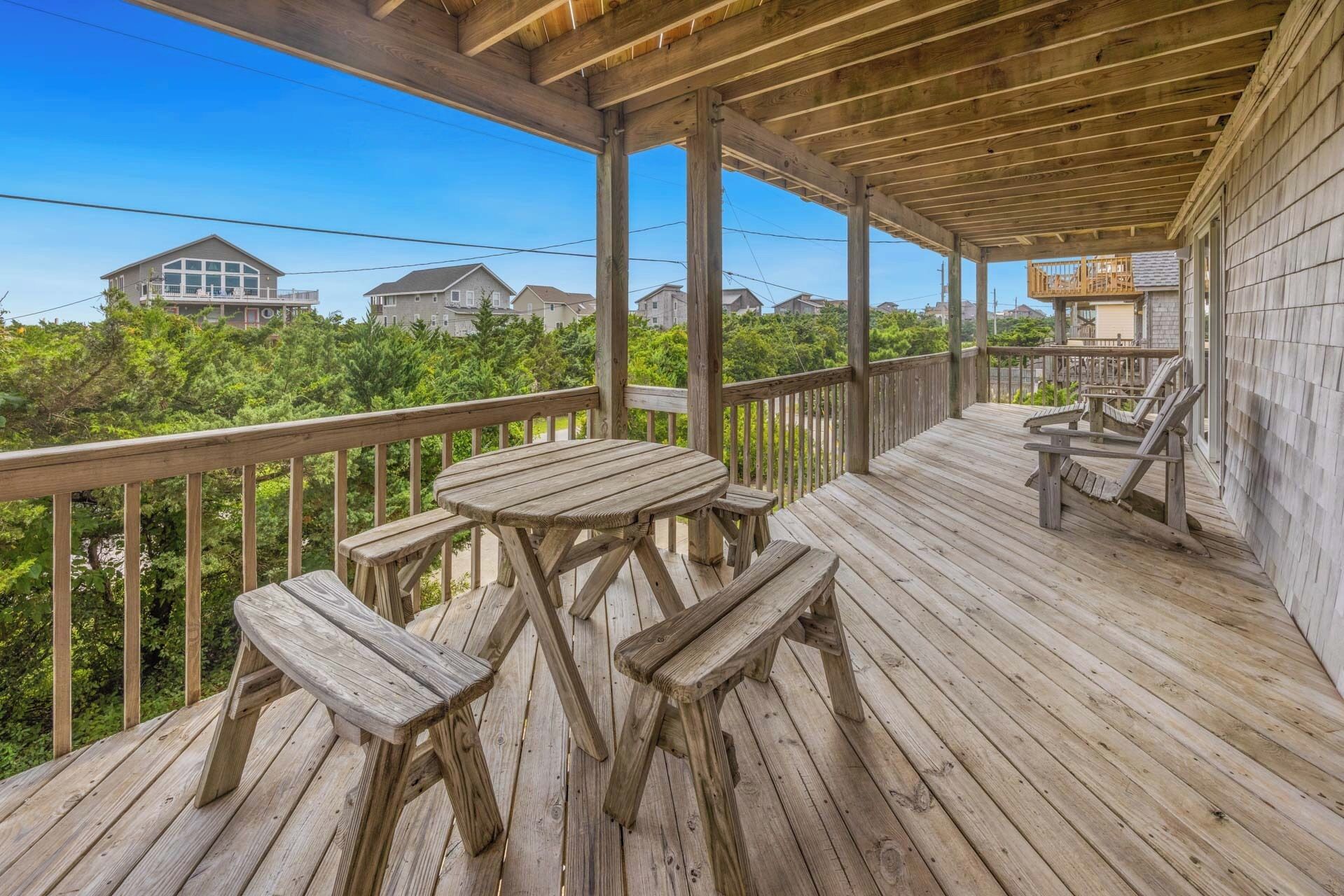 Une terrasse en bois, agrémentée de tables et de chaises pour pique-niquer, qui offre une vue sur un quartier résidentiel avec ses maisons et sa verdure.