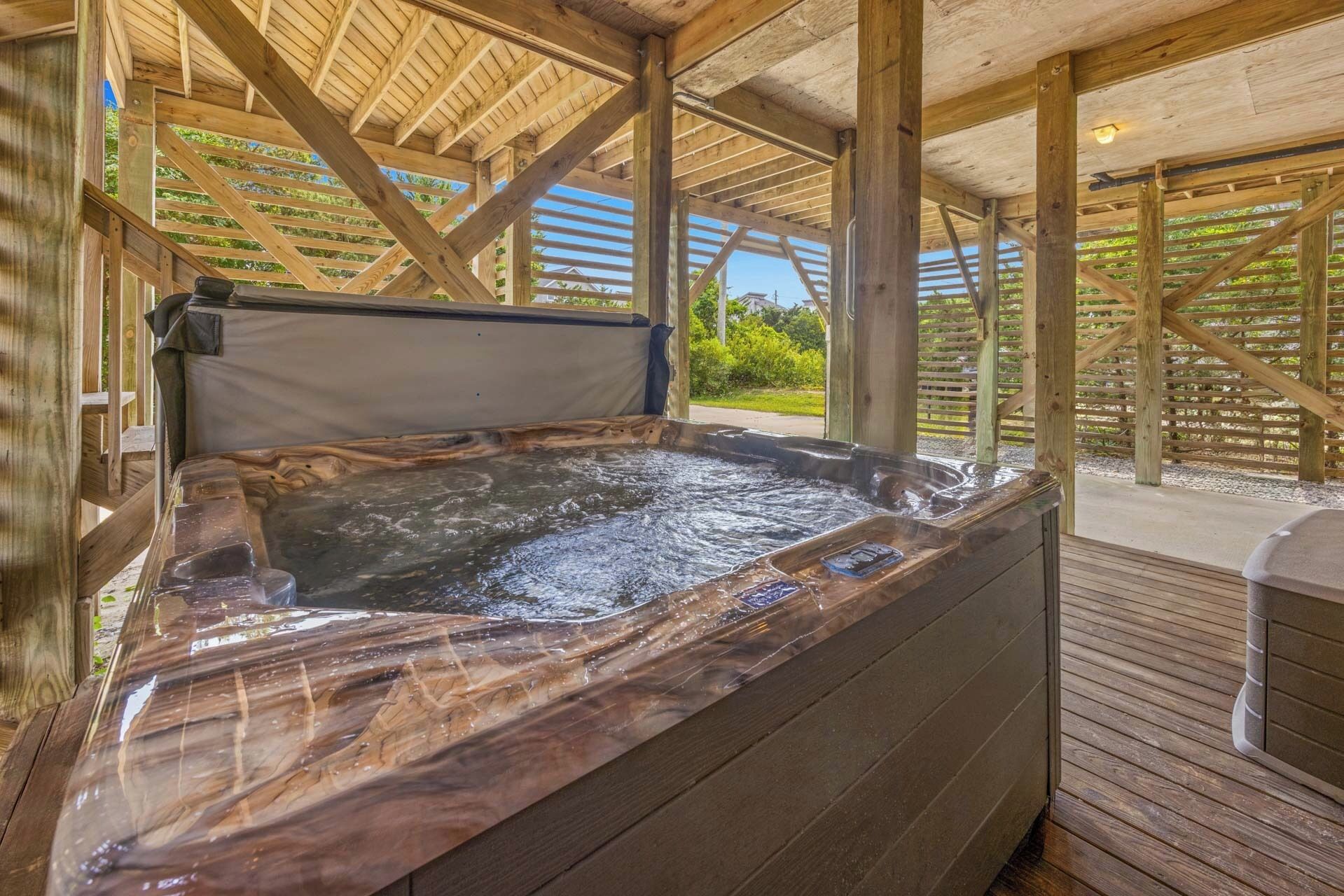 A hot tub with a wooden deck and a view of greenery.