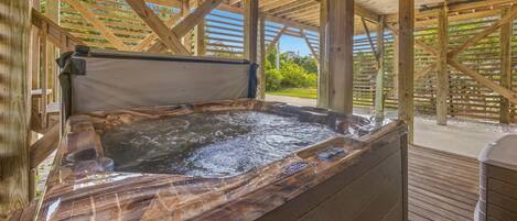 A hot tub with a wooden deck and a view of greenery.