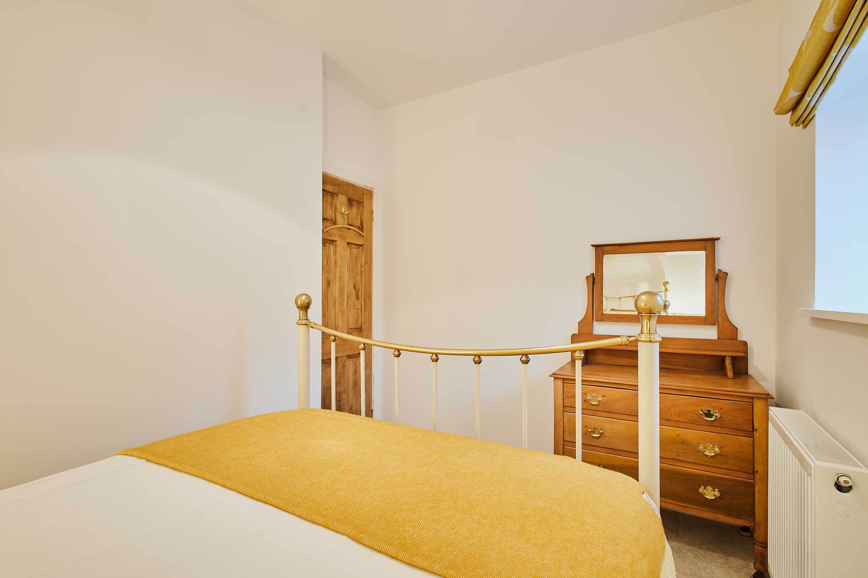 Un dormitorio con cama, cómoda de madera, espejo y radiador.