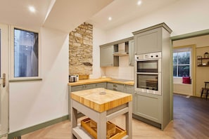 Une cuisine avec un mur d’accent en pierre, une table en bois et des appareils électroménagers intégrés.
