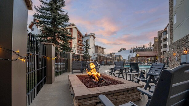 An outdoor seating area with a fire feature, surrounded by lounge chairs and a pool in the background. - Grand Lodge Studio 412 — Ski-In/Out Mt CB, Hot Tub & Pool, Pets OK (Crested Butte)