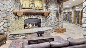 A stone fireplace with a log fire, a wooden bench, and a leather sofa in a lobby area. - Grand Lodge Studio 412 — Ski-In/Out Mt CB, Hot Tub & Pool, Pets OK (Crested Butte)