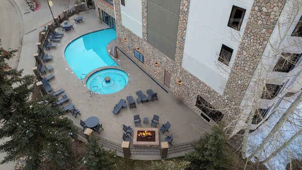 Un área de piscina en la azotea con sillones de descanso y una chimenea, rodeada de muros de piedra y un edificio con varias ventanas.