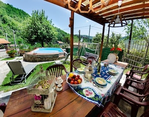 An outdoor dining area with a pool, wooden furniture, and a view of the surrounding greenery. - Cottage in San Marcello With Pool and Charm (San Marcello Piteglio)