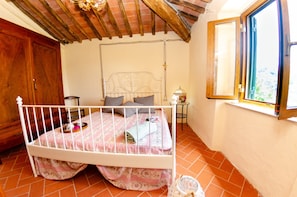 A bedroom with a white metal bed frame, a wooden wardrobe, a window with a view, and a tiled floor. - Cottage in San Marcello With Pool and Charm (San Marcello Piteglio)