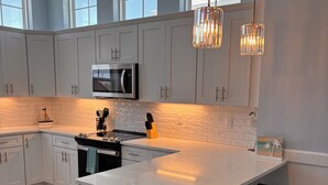 Una cocina moderna con armarios blancos, una isla central con taburetes de bar, un bote de basura de acero inoxidable e iluminación colgante.