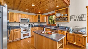 A modern kitchen with wooden cabinets, stainless steel appliances, and a central island with fruit.