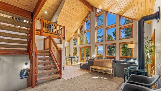 A spacious living area with a wooden staircase, large windows, and a fireplace.