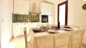 A dining area with a table set for four, white cabinets, a green tiled backsplash, and a clock on the wall. - Villas with common or private pool in Costa Rei (Muravera)