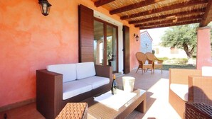 An outdoor seating area with wicker furniture, a white sofa, and a table with a bottle. - Villas with common or private pool in Costa Rei (Muravera)