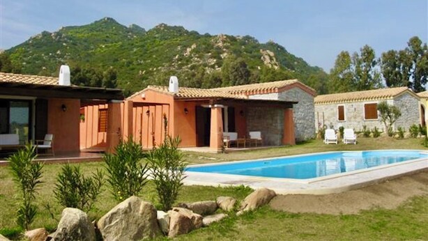 A villa with a swimming pool, stone walls, and a mountainous backdrop. - Villas with common or private pool in Costa Rei (Muravera)