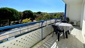Ein Balkon mit Tisch und Stühlen, einem blauen Geländer und Blick auf Bäume und Gebäude.