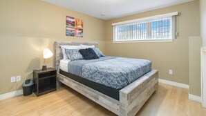 Een slaapkamer met een houten bed, een nachtkastje met een lamp, een raam met jaloezieën en een wand met drie ingelijste foto's.